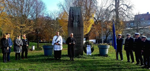 Mehrere Personen stehen neben einem Kriegsdenkmal