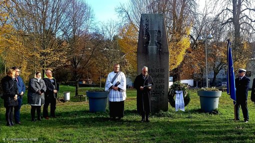 Mehrere Personen stehen neben einem Kriegsdenkmal