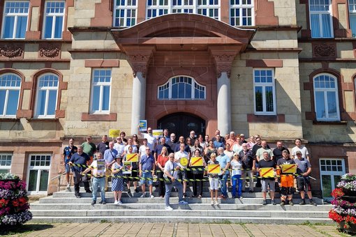 Stadtmitarbeiter stehen auf Rathaustreppe und schauen erbost. Schilder und Logos der Kampagne werden in  die Luft gehoben.