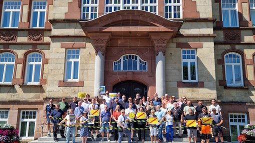 Stadtmitarbeiter stehen auf Rathaustreppe und schauen erbost. Schilder und Logos der Kampagne werden in  die Luft gehoben.