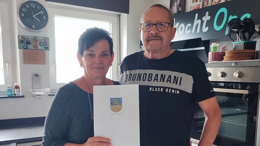 Ehepaar steht in Küche mit Stadt-Urkunde in der Hand 