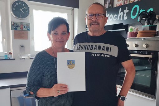 Ehepaar steht in Küche mit Stadt-Urkunde in der Hand