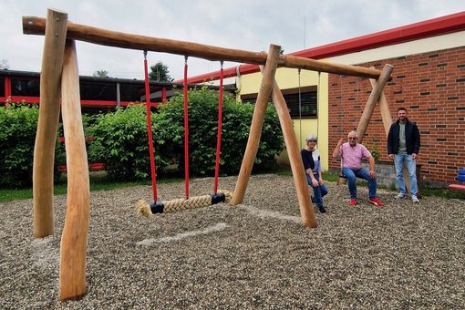 Frau und zwei Männer präsentieren die neue Kinderschaukel aus Holz