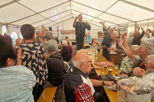 Der Sänger steht auf einer Bank im Festzelt, umgeben von feiernden Besuchern.