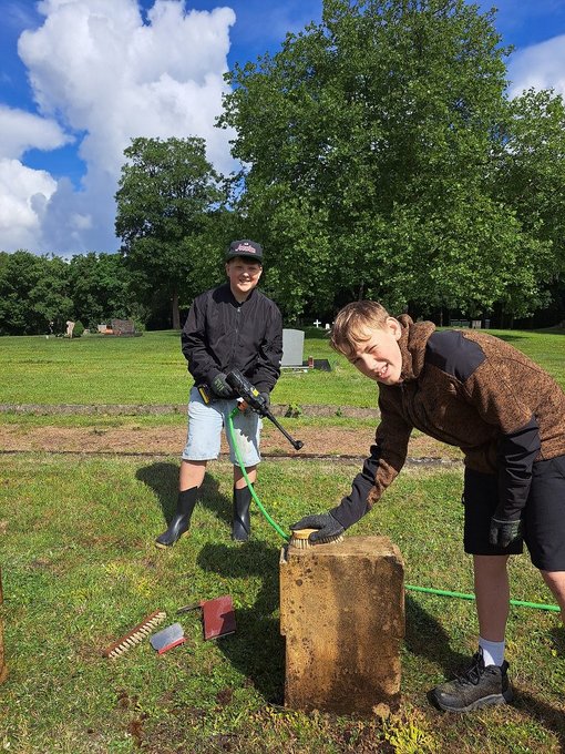 Zwei Schüler bei der Grabsteinpflege mit Bürste und Wasser