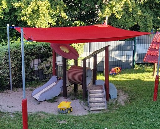 Rotes Sonnensegel über einen kleinen Spielplatz gespannt