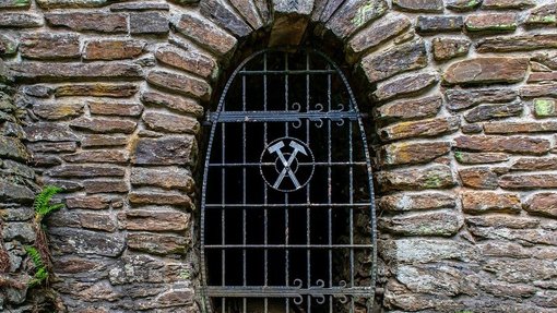 Gemauerter Grubenstollenmund versperrt durch ein Gitter mit Bergbauzeichen