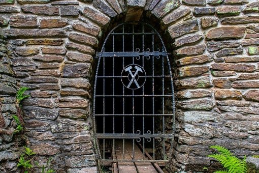 Gemauerter Grubenstollenmund versperrt durch ein Gitter mit Bergbauzeichen