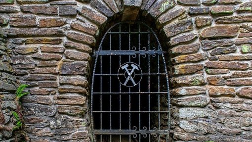 Gemauerter Grubenstollenmund versperrt durch ein Gitter mit Bergbauzeichen
