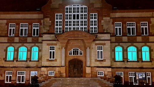 Fenster des Rathauses sind im Erdgeschoss grün beleuchtet, Blick vom Rathausvorplatz 