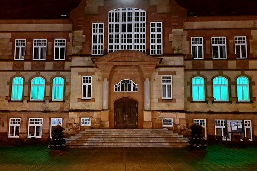 Fenster des Rathauses sind im Erdgeschoss grün beleuchtet, Blick vom Rathausvorplatz 