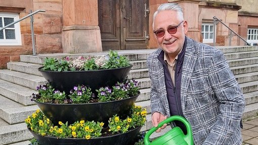 Bürgermeister gießt Blumenbett mit grüner Gießkanne