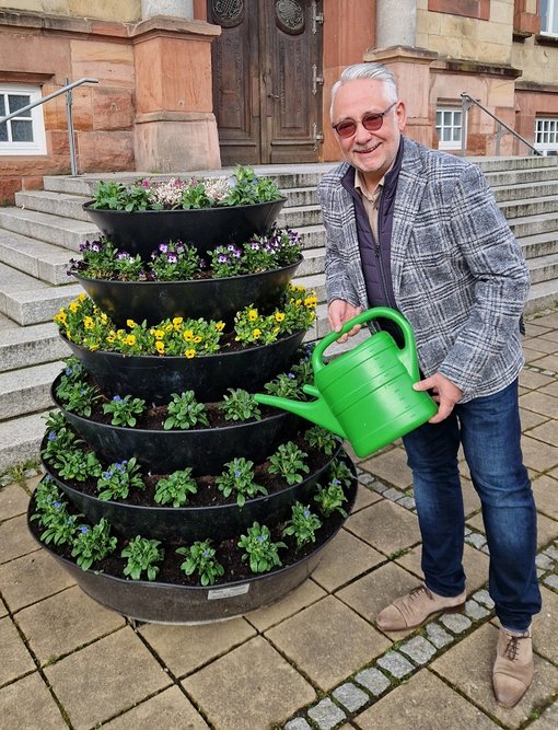 Bürgermeister gießt Blumenbett mit grüner Gießkanne